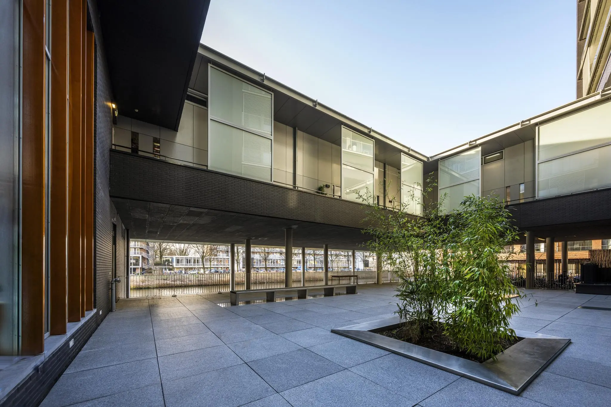 Binnenplaats op het George Gershwinplein met moderne architectuur, grote ramen en een plantenperk met bamboe.